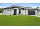 A modern home with white stucco, a gray roof, a dark garage door, and a green lawn at 2805 Anniston Rd, North Port, FL 34288