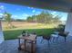 A covered patio with chairs, a small table, and a beverage cart overlooks a large grassy yard at 2726 Wise River Lane, Zephyrhills, FL 33539