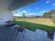 A covered patio with seating provides a view of the green lawn and distant treeline in this backyard at 2726 Wise River Lane, Zephyrhills, FL 33539