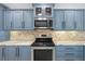 Up close kitchen features stainless steel appliances, stylish blue cabinets and stone tile backsplash at 5474 Dominica Cir, Sarasota, FL 34233