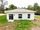 Back exterior of the home featuring sliding glass doors, a small patio, and two windows with lush green grass at 8990 Glenarm Way, Weeki Wachee, FL 34613