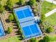 Aerial view of fenced in blue tennis courts surrounded by manicured landscaping and community green spaces at 1220 Tahitian Sunrise Dr, Plant City, FL 33565