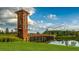 Community wooden entrance tower and bridge overlooking the pond with green grass and blue sky at 1570 Hubbell Rd, Wesley Chapel, FL 33543