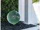 Close-up of a modern green glass ball nestled amid greenery and dark decorative stones at 3310 Sunset N Dr, St Petersburg, FL 33710