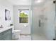 Modern bathroom with glass shower, white cabinets, and a window overlooking lush landscaping at 24145 Blackbeard Blvd, Punta Gorda, FL 33955