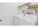 Bright laundry room featuring a white washer and dryer set with shelving, perfect for efficient home management at 2943 Willowleaf Ln, Wesley Chapel, FL 33544
