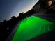 Dusk view of a swimming pool with bright green lighting and a house in the background at 821 Silver Springs Nw Ter, Port Charlotte, FL 33948