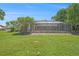 View of the backyard with a screened-in pool area, lawn, and mature trees at 2435 Hawk Griffin Rd, Plant City, FL 33565