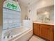 Bright bathroom with a soaking tub under a stained-glass window and a wooden vanity with a large mirror at 1913 Blue River Rd, Holiday, FL 34691