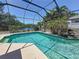 Clear blue pool with a decorative waterfall feature, set in a screened-in enclosure with scenic views at 1913 Blue River Rd, Holiday, FL 34691
