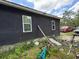 Side view of the house showing exterior wall, windows, and overgrown yard with bikes and miscellaneous items at 3613 Deleuil Ave, Tampa, FL 33610