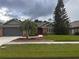Charming single-Gathering home featuring a red door, well-manicured lawn, and mature trees under a cloudy sky at 1403 Ventana Dr, Sun City Center, FL 33573