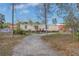 Exterior view of a single-story home with a gravel driveway, and a small porch, set against a backdrop of trees at 8279 Sunshine Grove Rd, Brooksville, FL 34613