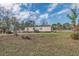 Wide exterior shot showcases the single-story home, surrounded by green grass and scattered trees against a blue sky at 8279 Sunshine Grove Rd, Brooksville, FL 34613