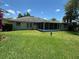 An exterior view of the home showcasing a spacious yard with lush green grass, mature landscaping, and screened-in patio at 9685 Southern Belle Dr, Weeki Wachee, FL 34613