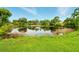 A calm pond reflects the surrounding trees and foliage, with a neatly mowed lawn in the foreground at 5728 Colonial Dr, New Port Richey, FL 34653