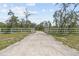 Long private driveway leading to a gated entrance, surrounded by a white fence at 10230 289Th E St, Myakka City, FL 34251