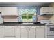 A bright kitchen featuring white cabinetry and a sink under a window with patterned curtains at 304 Highland St, Brooksville, FL 34601