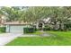 Inviting home featuring a two-car garage, mature trees, lush landscaping, and a green front lawn at 2332 Timbergrove Dr, Valrico, FL 33596