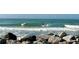Active ocean scene showing surfers riding waves, with a rocky shoreline in the foreground at 468 Ceil Dr, Nokomis, FL 34275