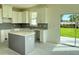 Modern kitchen featuring white cabinets, a gray island, and stainless steel appliances, with backyard views at 13610 Wolfpack Rd, Hudson, FL 34667