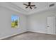This bedroom features neutral walls, a modern ceiling fan, and a bright window with tropical landscaping views at 8489 Topeka Cir, Port Charlotte, FL 33981
