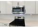Close-up view of new stainless steel stove and microwave oven with white cabinets and subway tile backsplash at 9071 Players Dr, Weeki Wachee, FL 34613