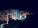 Night view of well-lit condo buildings, pool, palm trees, and manicured landscaping at 6009 Sea Ranch Dr # 101, Hudson, FL 34667