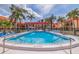 Community pool and lounge area with chairs, tables, and umbrellas surrounded by beautiful landscaping and palm trees at 10365 Paradise Blvd # 21, Treasure Island, FL 33706