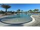 Expansive community pool with ample lounge seating, palm trees, and a waterfall feature under a bright blue sky at 14553 Eagle Branch Dr, Nokomis, FL 34275