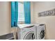 Bright laundry room featuring a modern washer and dryer set, complemented by a window with blue curtains at 6932 Gray Catbird Loop, Wesley Chapel, FL 33545