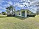 Charming green home boasts an expansive lawn, complemented by swaying palm trees under a bright sky at 1718 Trailwater St, Ruskin, FL 33570