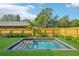 Backyard swimming pool surrounded by green grass, a wooden fence, and manicured shrubbery at 1630 Douglas Ave, Dunedin, FL 34698