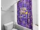 Bathroom with purple and gold LSU-themed shower curtain, toilet, and white tiled walls at 11946 Brighton Knoll Loop, Riverview, FL 33579