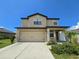 Two-story house featuring a tan exterior, two-car garage, and landscaping at 6949 Crested Orchid Dr, Brooksville, FL 34602