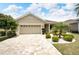 Tan house with a three-car garage, landscaping, and a paved driveway at 1013 Emerald Dunes Dr, Sun City Center, FL 33573