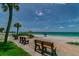 Scenic view of a beach with benches, palm trees, and clear turquoise water under a blue sky at 221 Howard Dr, Belleair Beach, FL 33786