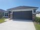 Inviting home featuring a dark gray garage door, gray siding, and a well-manicured lawn with young palm trees at 13260 Ogden Glade Rd, Dade City, FL 33525