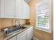 Laundry sink with white cabinets, countertop, and a window with shutters at 13216 Legends Trl, Dade City, FL 33525