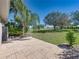 Open brick patio with a view of the expansive, green backyard with mature trees and landscaping at 13216 Legends Trl, Dade City, FL 33525