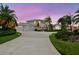 Stunning waterfront home boasts a three-car garage, mature palms, and circular driveway, all set against a colorful sky at 5709 E Longboat Blvd, Tampa, FL 33615
