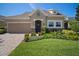Tan house with a stone facade, two-car garage, and manicured landscaping at 13939 Swallow Hill Dr, Lithia, FL 33547