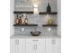 Stylish wet bar featuring floating shelves, mosaic backsplash, and elegant countertop with stainless sink and white cabinets at 8716 Elmwood Ln, Tampa, FL 33615