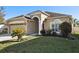 Tan house with red door, two car garage, and landscaped yard at 7720 Rathdown Ln, Wesley Chapel, FL 33545