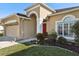 Tan house with red door, two car garage, and landscaped yard at 7720 Rathdown Ln, Wesley Chapel, FL 33545