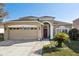 Tan house with red door, two car garage, and landscaped yard at 7720 Rathdown Ln, Wesley Chapel, FL 33545