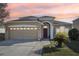 Tan house with red door, two car garage, and landscaped yard at 7720 Rathdown Ln, Wesley Chapel, FL 33545