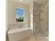 Bright bathroom with a soaking tub beneath a window, complemented by a tiled shower and marble accent wall at 15154 Appleton Blvd, Port Charlotte, FL 33981