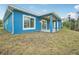 Backyard view of a vibrant blue house with a covered patio and well-maintained lawn at 272 Diogenes St, Dunedin, FL 34698