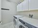 Bright laundry room features modern washer and dryer, storage cabinets, and a convenient hook rack at 16850 Whisper Elm St, Wimauma, FL 33598